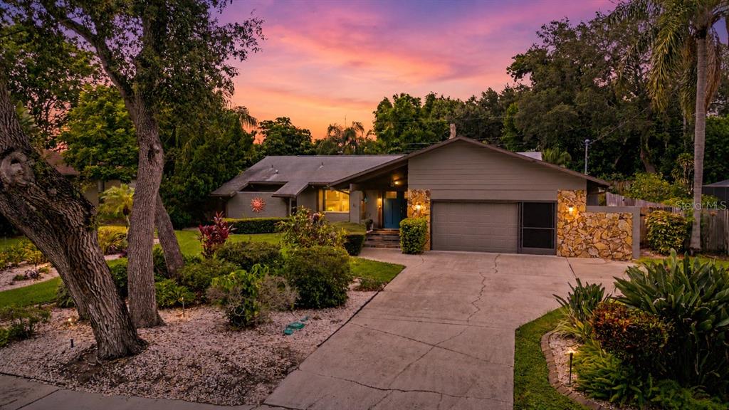 A single-story house with a stone facade, a concrete driveway, and a sunset sky background — 1706 AVOCA DRIVE, TARPON SPRINGS, FL