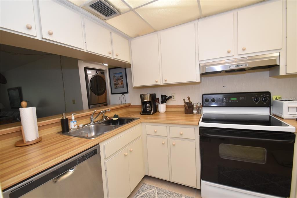 A kitchen features white cabinets, wood-look laminate countertops, a stainless steel dishwasher, and a stove — 1709 PELICAN COVE ROAD UNIT GL349, SARASOTA, FL