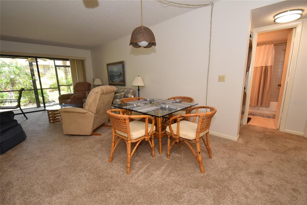 A dining area with a glass-topped rattan table sits adjacent to a living room — 1709 PELICAN COVE ROAD UNIT GL349, SARASOTA, FL