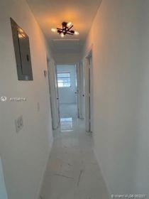 A narrow hallway with white walls, light-colored tile flooring, and a modern ceiling light fixture — 751 NW 18 Street, Pompano Beach FL 33060, POMPANO BEACH, FL