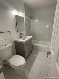 A modern bathroom features a gray vanity, a white toilet, and a tiled shower-tub combination — 751 NW 18 Street, Pompano Beach FL 33060, POMPANO BEACH, FL