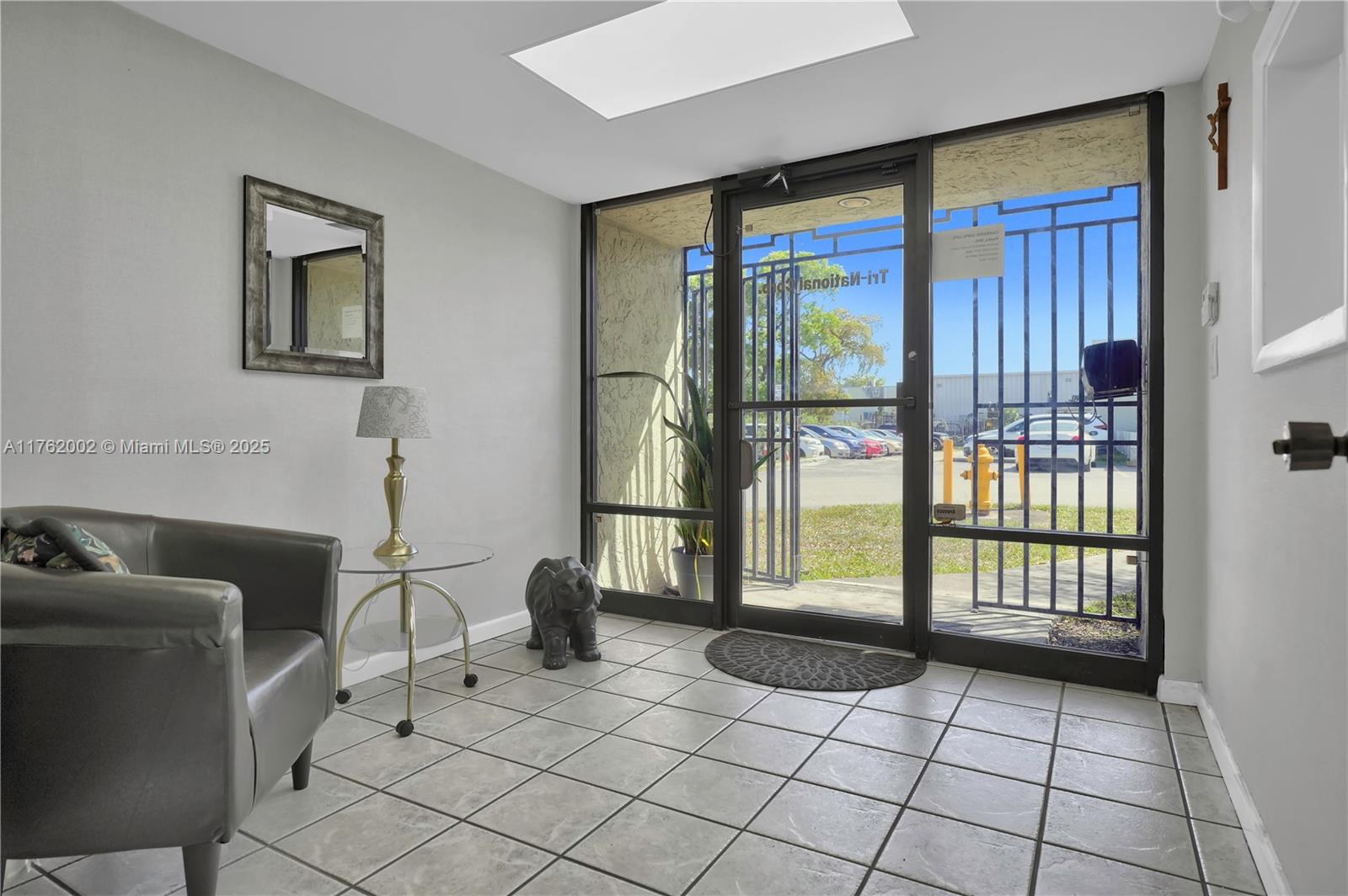 A tiled entryway features a gray armchair, a glass side table, and a glass-paneled door — 5220 NW 72nd Ave # A1, Miami FL 33166, MIAMI, FL