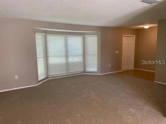 An empty room with beige carpet, light-colored walls, and a large bay window with blinds — 3654 PIN OAKS STREET, SARASOTA, FL