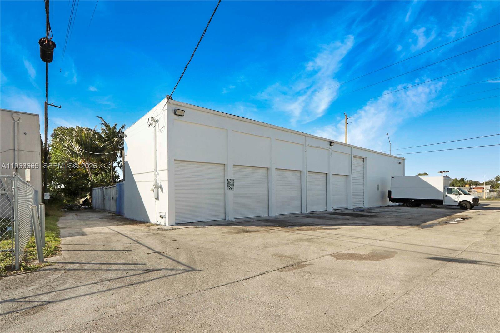 A white industrial warehouse building features multiple roll-up doors and a large paved parking lot — 9795 NW 7th Ave, Miami FL 33150, MIAMI, FL