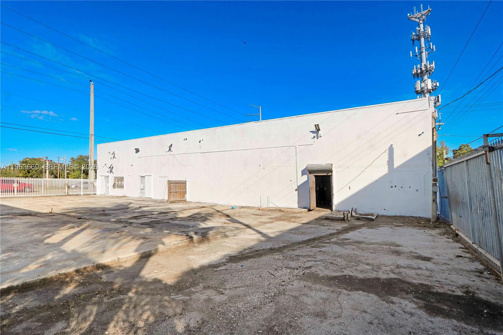 A white industrial building exterior features a concrete lot, a metal door, and a cell tower — 9795 NW 7th Ave, Miami FL 33150, MIAMI, FL