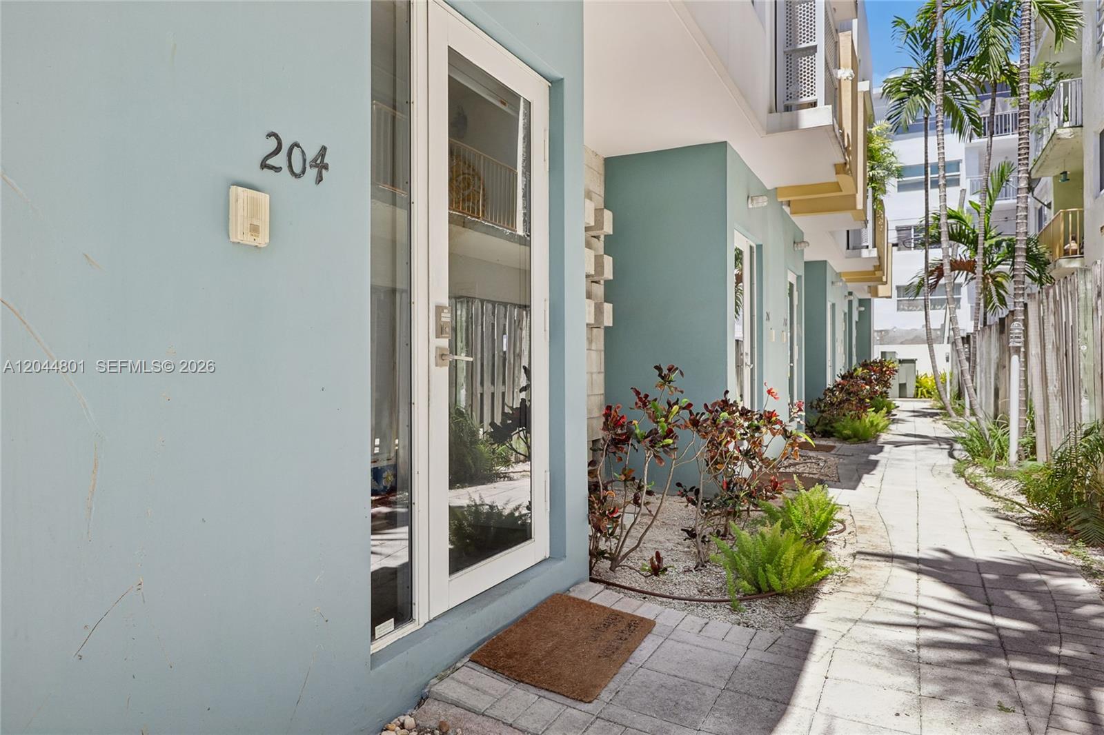 The exterior of a light blue building features a glass door labeled 204 and landscaping — 204 Washington Ave # 13, Miami Beach FL 33139, MIAMI BEACH, FL