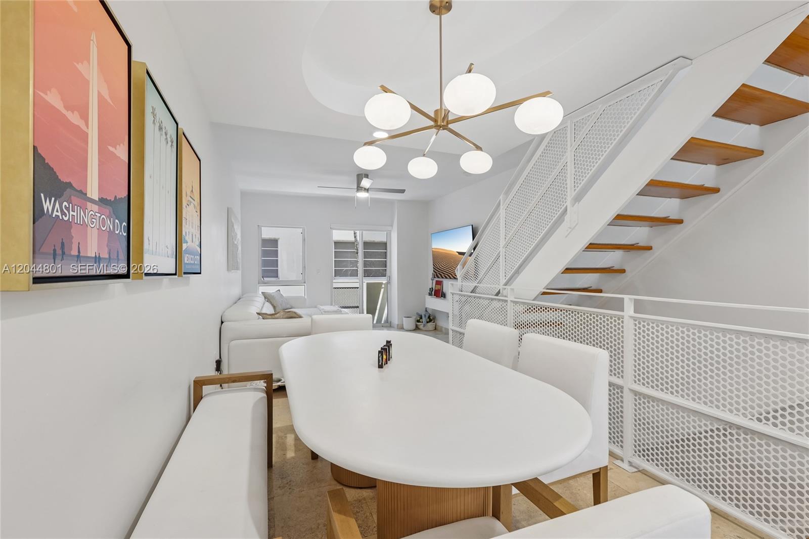 A dining area features a white oval table, modern chandelier, and stairs with white railings — 204 Washington Ave # 13, Miami Beach FL 33139, MIAMI BEACH, FL