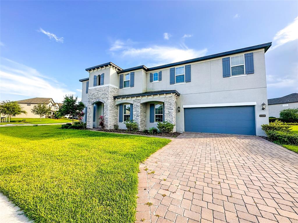 A two-story house with a stone facade, blue garage door, and a paved driveway — 1450 JUNIPER HAMMOCK STREET, WINTER GARDEN, FL