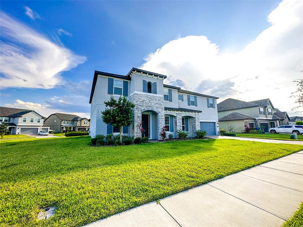 A two-story suburban house with a stone facade, gray stucco, and a green lawn — 1450 JUNIPER HAMMOCK STREET, WINTER GARDEN, FL
