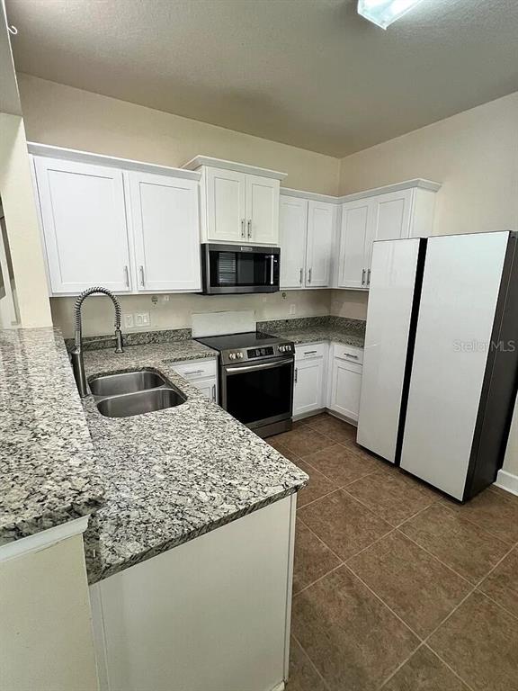 A kitchen features white cabinets, granite countertops, stainless steel appliances, and tile flooring — 6058 TWAIN STREET UNIT 101, ORLANDO, FL