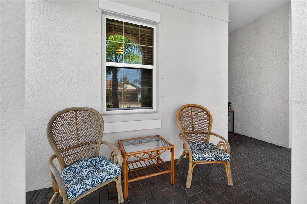 Two wicker chairs and a glass-topped table sit on a brick patio by a window — 17212 HOLLY WELL AVENUE, WIMAUMA, FL