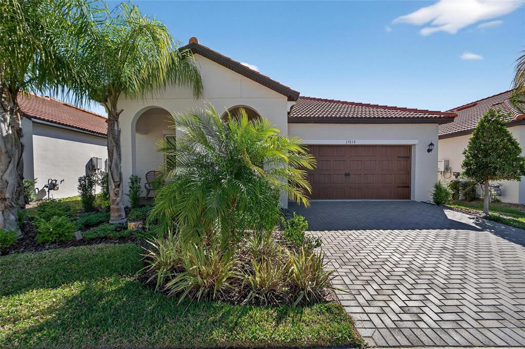 A single-story house with a brown garage door, tiled roof, and palm trees in front — 17212 HOLLY WELL AVENUE, WIMAUMA, FL