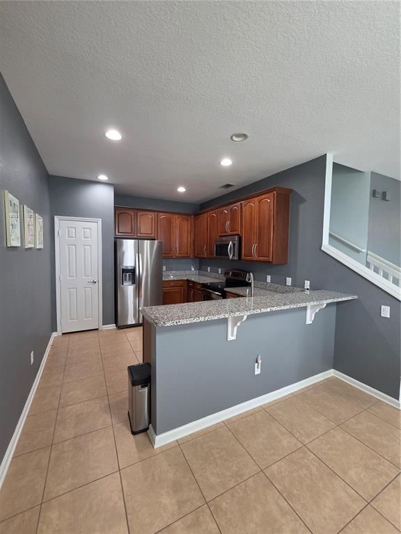 A kitchen features dark gray walls, wood cabinets, granite countertops, and stainless steel appliances — 1615 CROYDON STREET, ORLANDO, FL