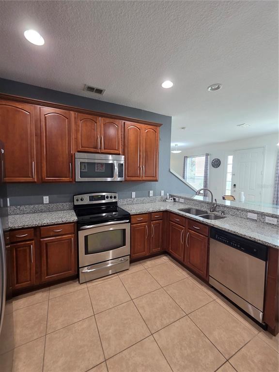 A kitchen features wood cabinets, granite countertops, stainless steel appliances, and beige tile flooring — 1615 CROYDON STREET, ORLANDO, FL