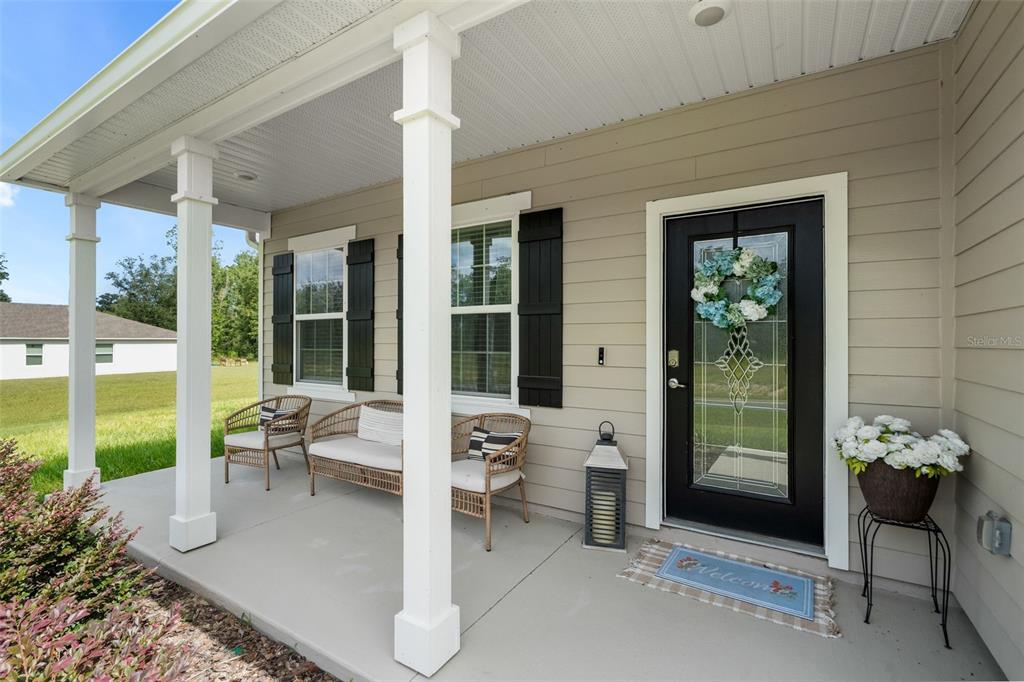 A covered front porch features wicker furniture, a black front door, and a welcome mat — 218 SW CADENCE GLEN, LAKE CITY, FL