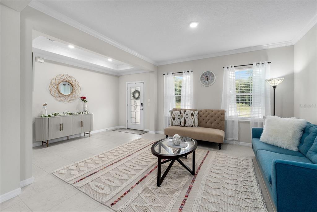 A living room features light tile floors, a blue sofa, a tan settee, and a rug — 218 SW CADENCE GLEN, LAKE CITY, FL