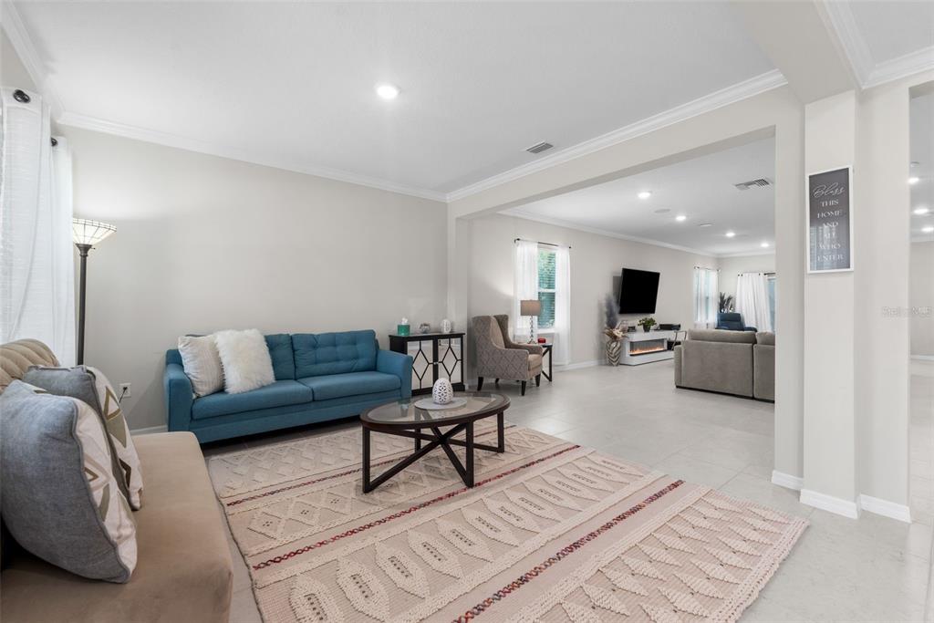 A living room features a blue sofa, a patterned area rug, and an adjacent den — 218 SW CADENCE GLEN, LAKE CITY, FL