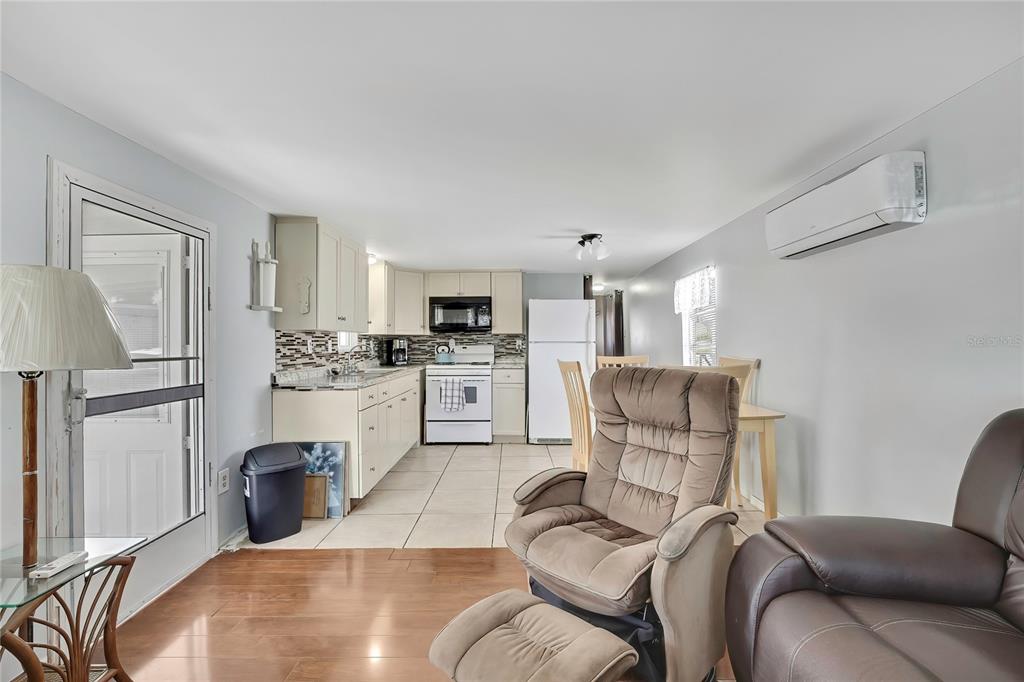 A kitchen with white cabinets and appliances opens into a living area with a recliner — 770 32ND AVENUE S UNIT 522, ST PETERSBURG, FL