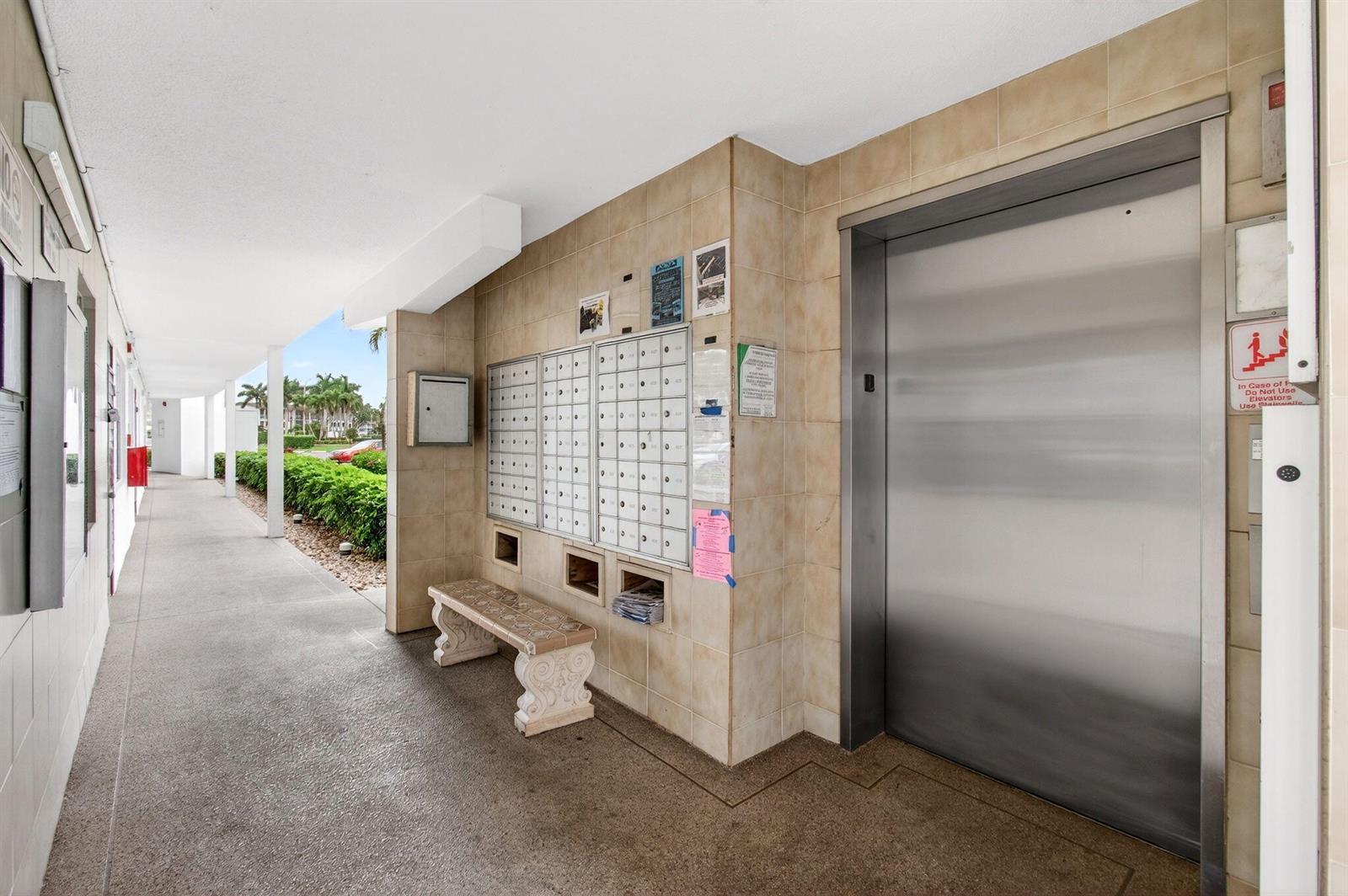 An outdoor hallway features a row of mailboxes, a stone bench, and an elevator — 3010 Guildford A, Boca Raton FL 33434, BOCA RATON, FL