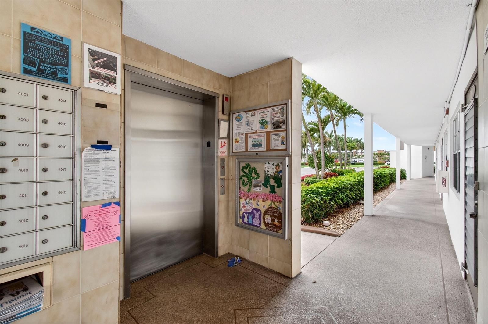 An outdoor hallway features a stainless steel elevator, a bank of mailboxes, and community bulletin boards — 3010 Guildford A, Boca Raton FL 33434, BOCA RATON, FL