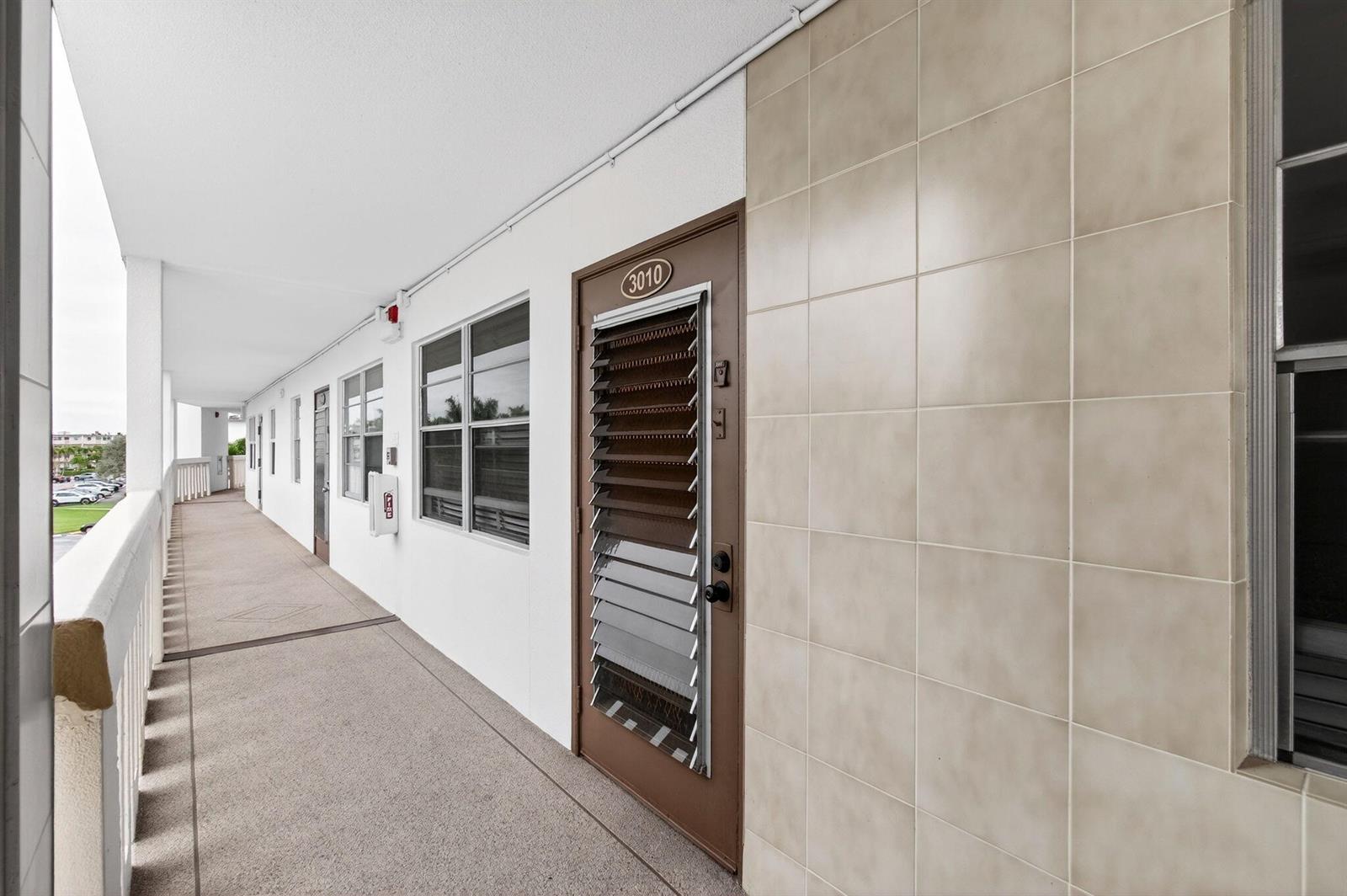 An outdoor apartment building walkway features a brown door numbered 3010 with a louvered insert — 3010 Guildford A, Boca Raton FL 33434, BOCA RATON, FL