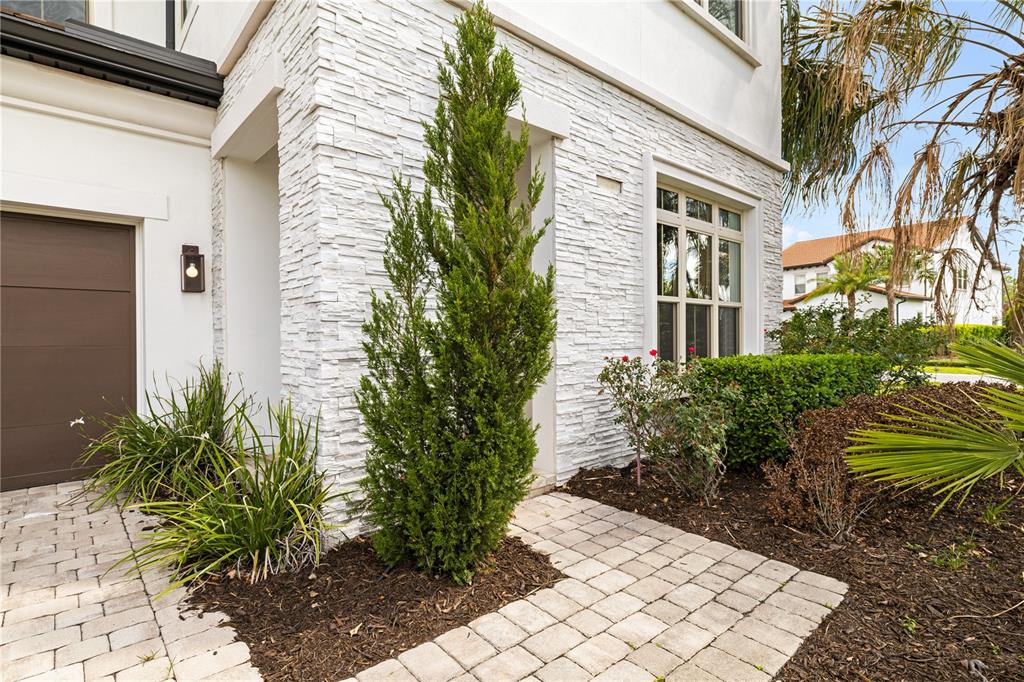 A white stone-clad house exterior features a tall evergreen tree and a paved walkway — 10829 ROYAL CYPRESS WAY, ORLANDO, FL