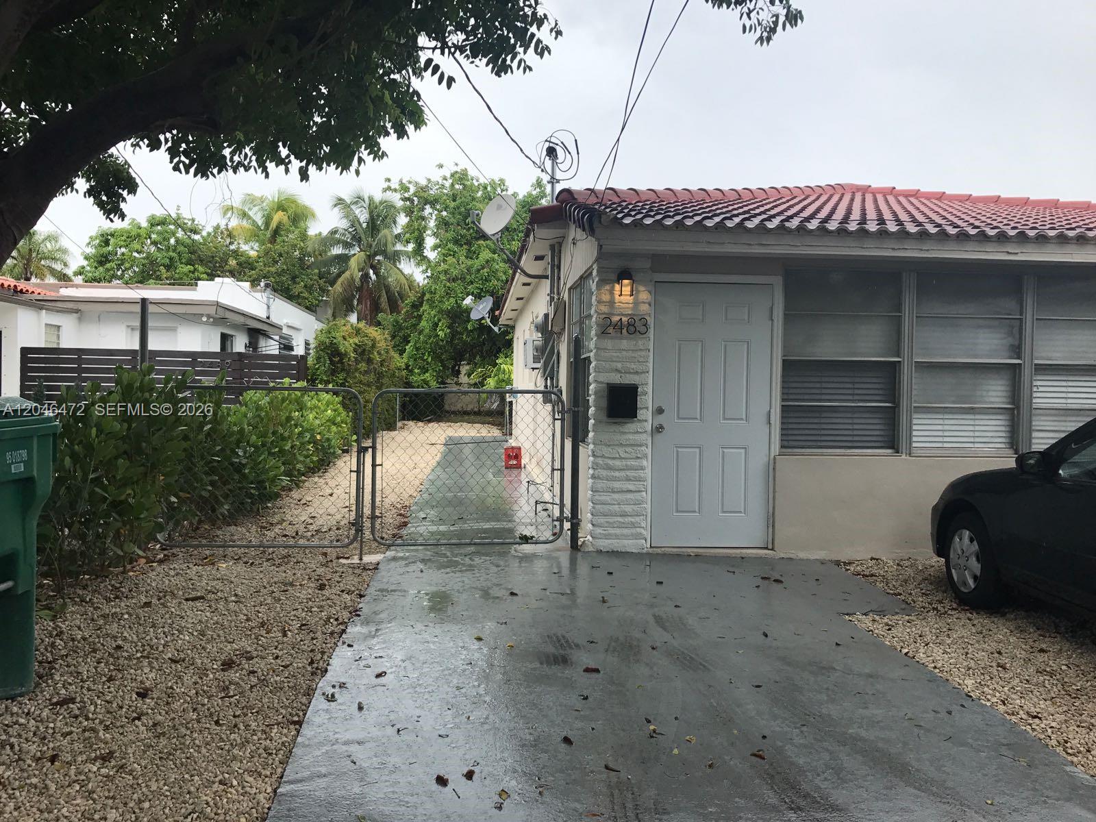 A white house with a red tile roof features a gated driveway and front entrance — MIAMI, FL