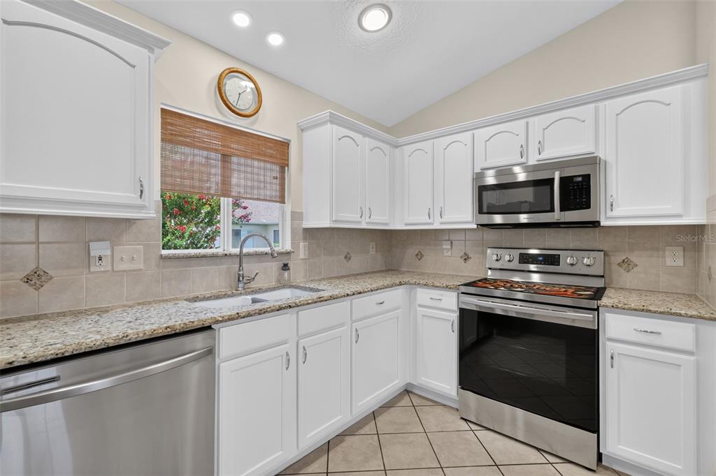 A kitchen with white cabinets, granite countertops, stainless steel appliances, and a window above the sink — 13902 SE 85TH COURT, SUMMERFIELD, FL