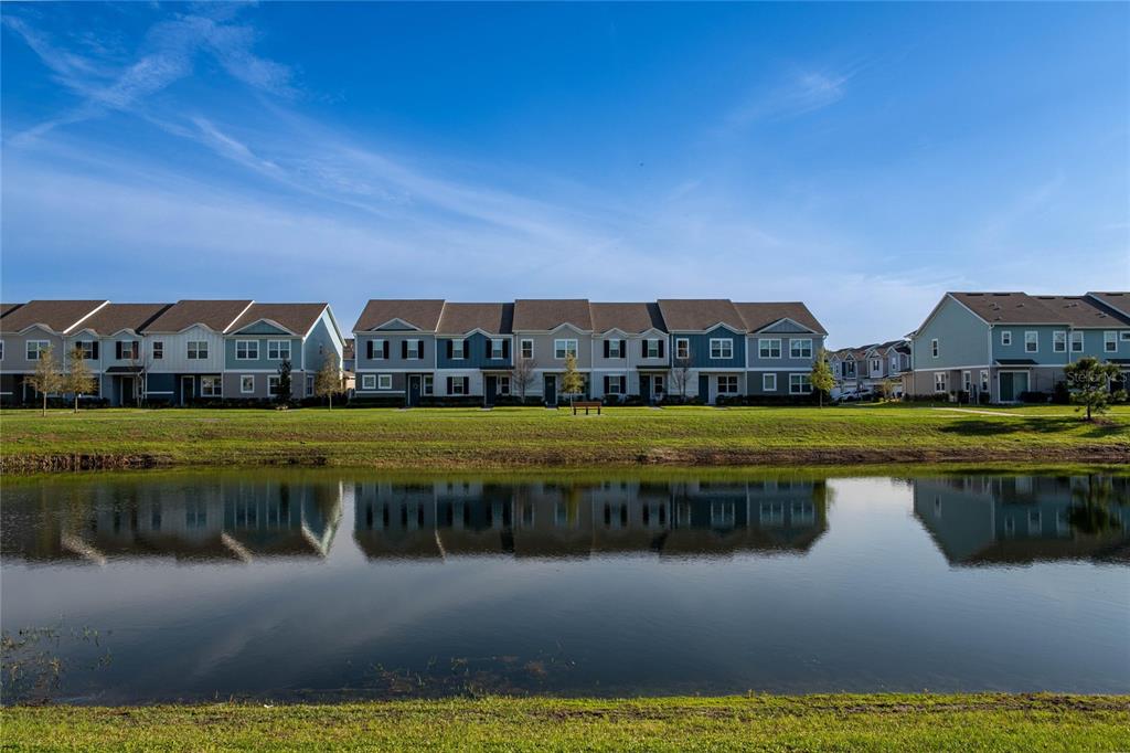 A row of townhouses sits behind a pond under a clear blue sky — 5222 FERNDALE ALLEY, ST CLOUD, FL