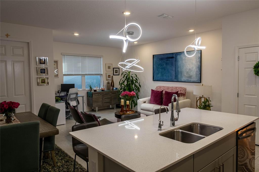 An open-concept kitchen with a quartz island overlooks a living area with modern pendant lights — 5222 FERNDALE ALLEY, ST CLOUD, FL