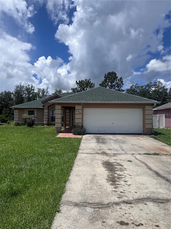 A single-story house with a green shingled roof, tan stucco exterior, and a concrete driveway — 338 KINGFISH DRIVE, KISSIMMEE, FL