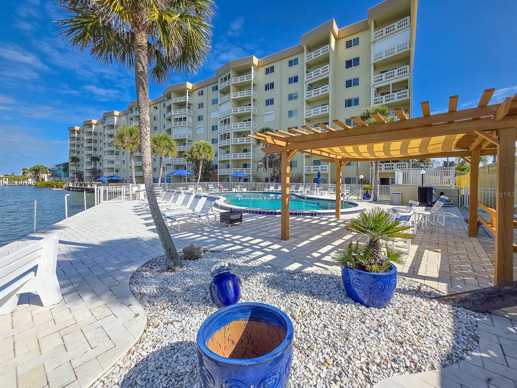 A swimming pool sits on a paved patio next to a multi-story building and pergola — 3606 S PENINSULA DRIVE UNIT 614, PORT ORANGE, FL