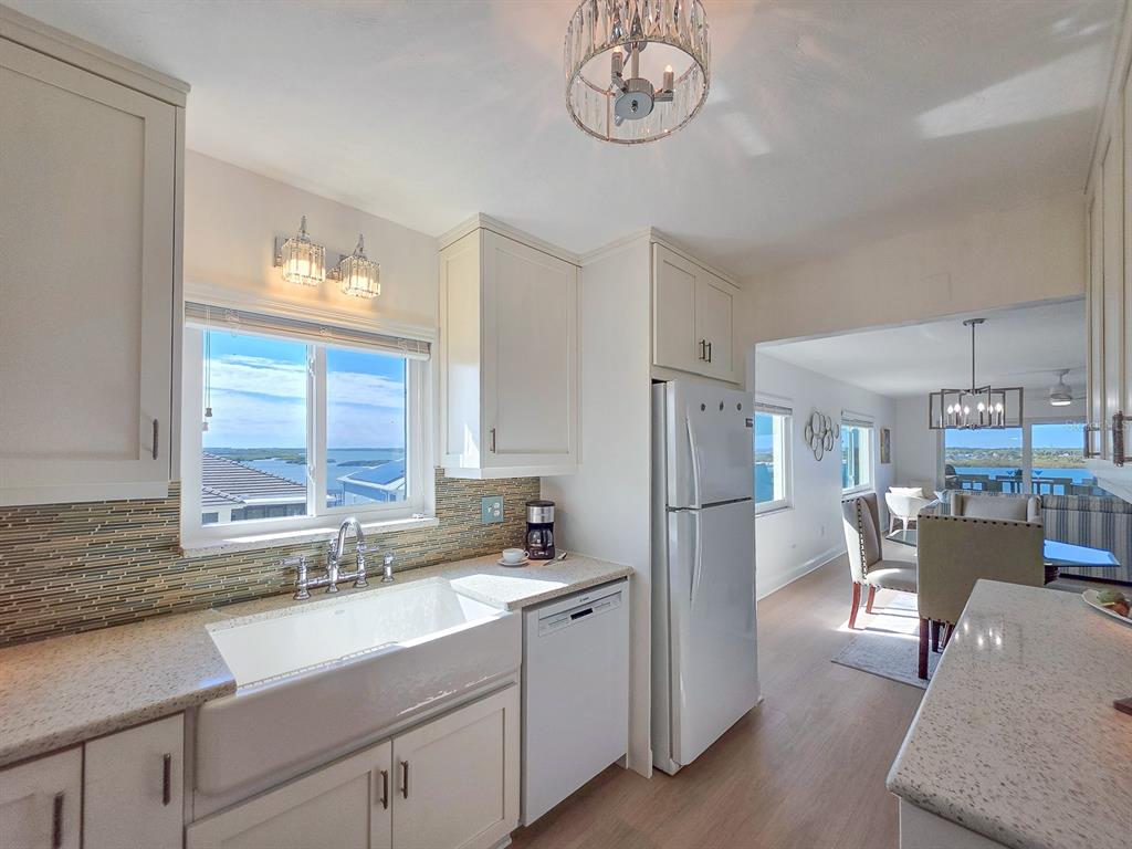 A white kitchen features a farmhouse sink, stone countertops, and a view of the water — 3606 S PENINSULA DRIVE UNIT 614, PORT ORANGE, FL