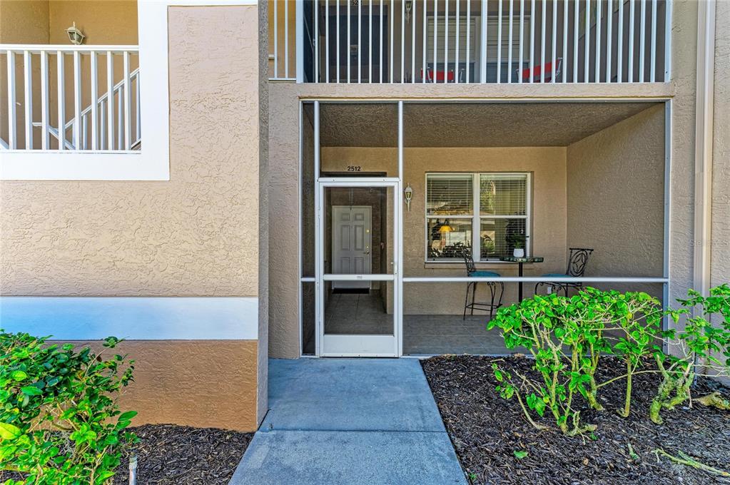A ground-level apartment entrance features a screened-in patio, a white front door, and beige stucco walls — 5350 HYLAND HILLS AVENUE UNIT 2512, SARASOTA, FL