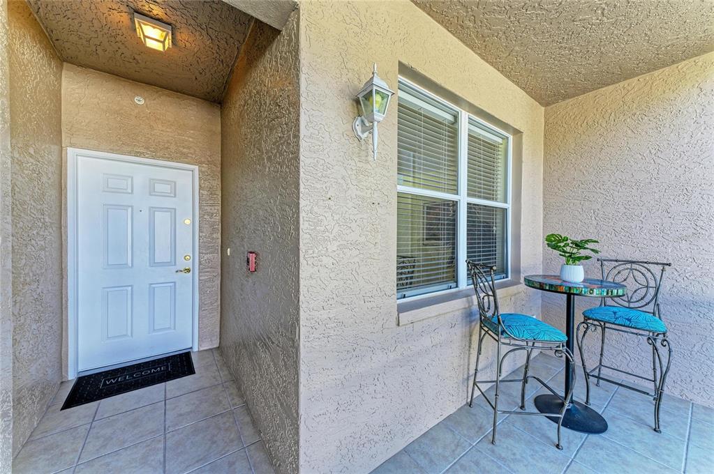 A covered entryway features a white front door, tiled floor, and a small bistro set — 5350 HYLAND HILLS AVENUE UNIT 2512, SARASOTA, FL
