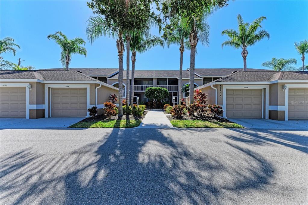 A two-story residential building features tan stucco walls, three garage doors, and palm trees — 5350 HYLAND HILLS AVENUE UNIT 2512, SARASOTA, FL