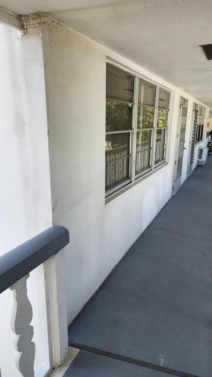 An exterior walkway with white walls, a gray floor, and several windows and doors — 96 Andover D, West Palm Beach FL 33417, WEST PALM BEACH, FL