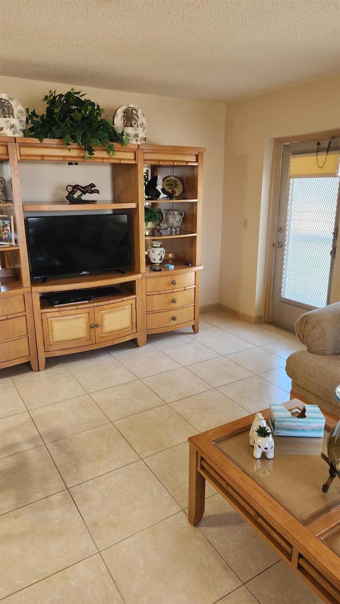 A living room features a large wooden entertainment center, tile flooring, and a glass-topped coffee table — 96 Andover D, West Palm Beach FL 33417, WEST PALM BEACH, FL