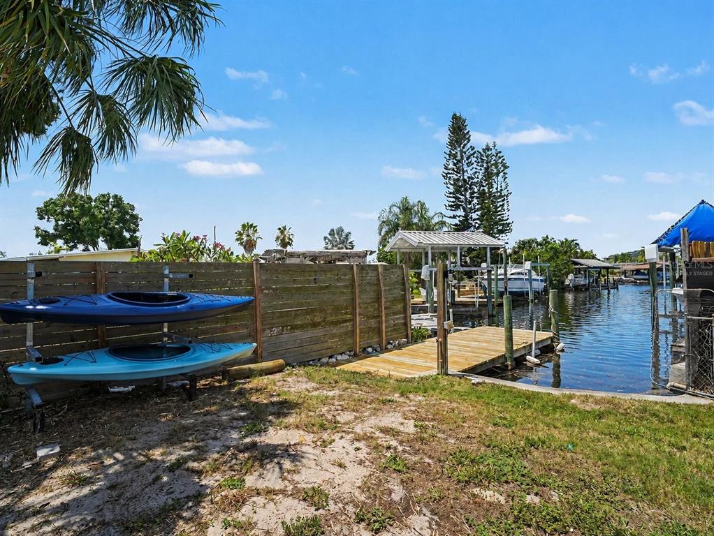 A wooden fence separates a sandy yard with two kayaks from a private boat dock — 802 WHITE HERON BOULEVARD, RUSKIN, FL