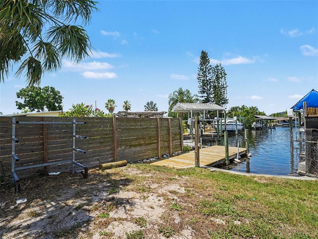 A wooden fence stands beside a small boat dock on a canal under a blue sky — 802 WHITE HERON BOULEVARD, RUSKIN, FL