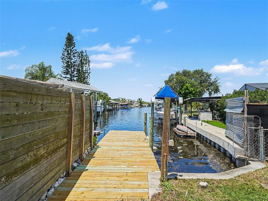 A wooden dock extends into a canal lined with boat slips and residential properties — 802 WHITE HERON BOULEVARD, RUSKIN, FL