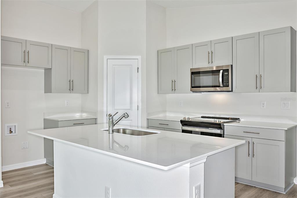 A modern kitchen features light gray cabinets, white countertops, a central island, and stainless appliances — 4607 HIKERS DRIVE, DAVENPORT, FL