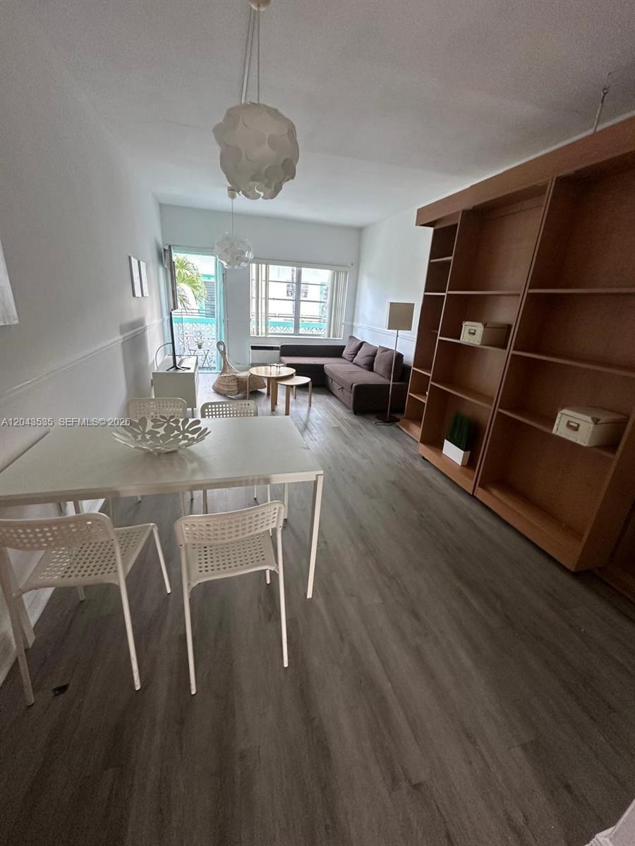 This living and dining area features wood-look flooring, a large bookshelf, and a balcony entrance — 6498 Collins Ave # 48, Miami Beach FL 33141, MIAMI BEACH, FL
