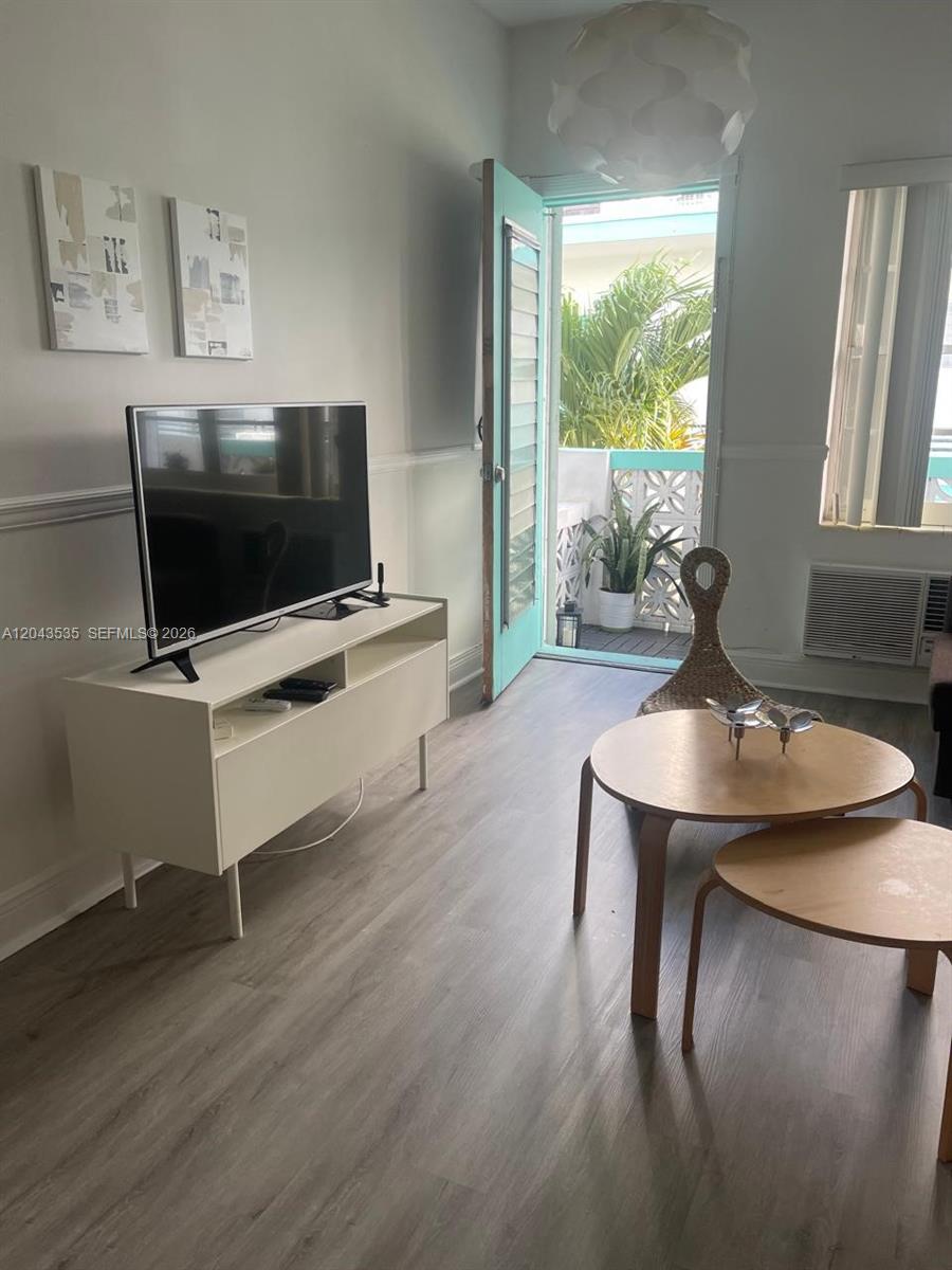 A living room features light wood flooring, a television console, and a door to a balcony — 6498 Collins Ave # 48, Miami Beach FL 33141, MIAMI BEACH, FL