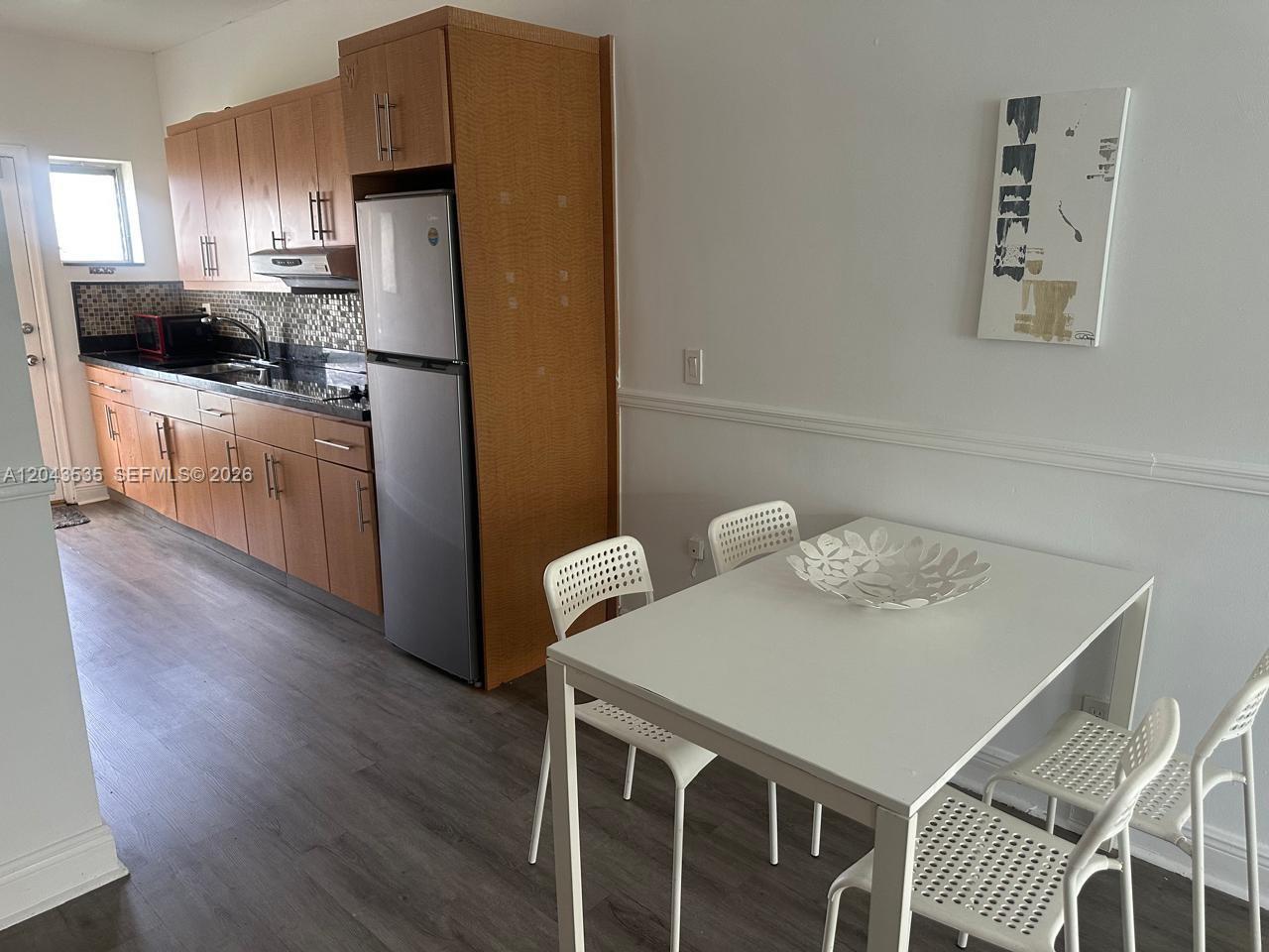 A kitchen with wood cabinets and stainless steel appliances sits next to a dining area — 6498 Collins Ave # 48, Miami Beach FL 33141, MIAMI BEACH, FL