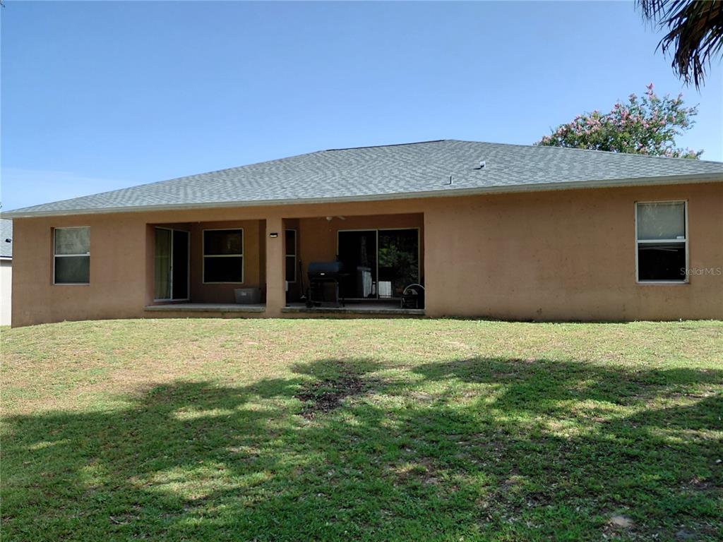 The rear exterior of a single-story house features a covered patio and a grassy yard — 2716 NE 24TH PLACE, OCALA, FL