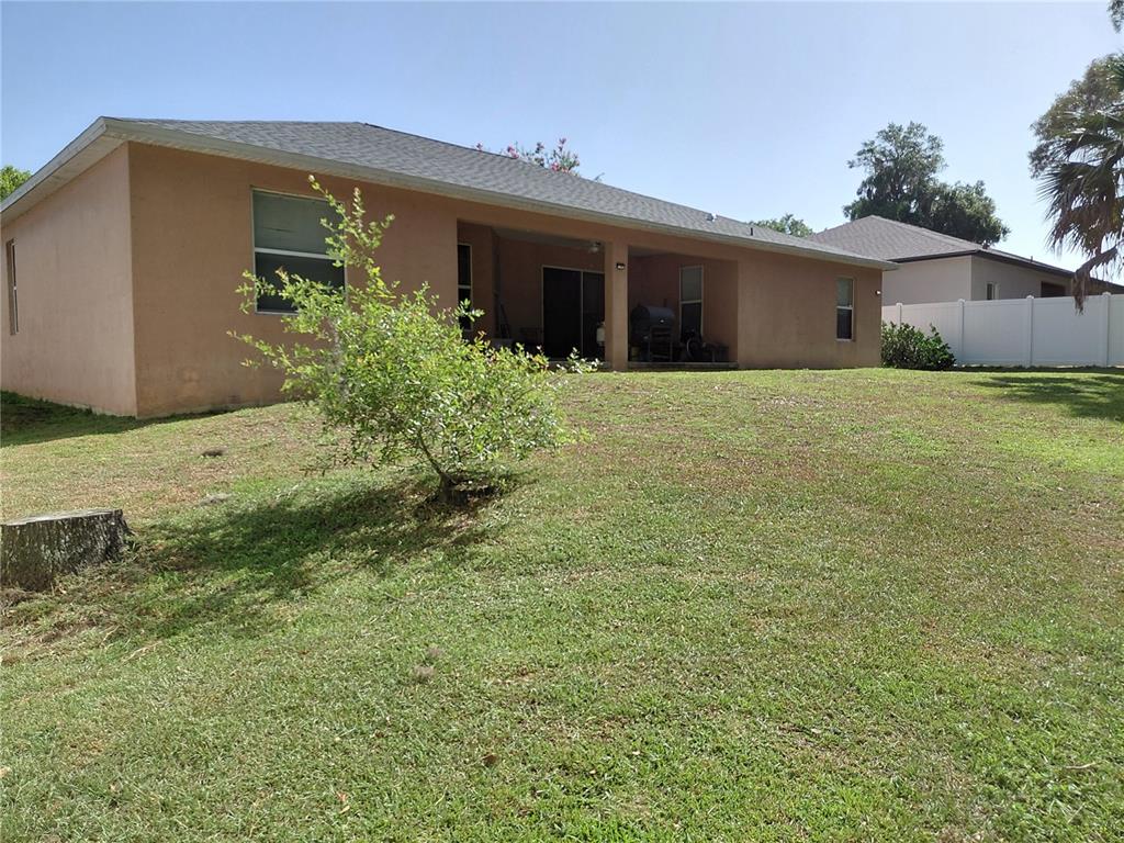 The rear exterior of a tan stucco house features a covered patio and grassy yard — 2716 NE 24TH PLACE, OCALA, FL