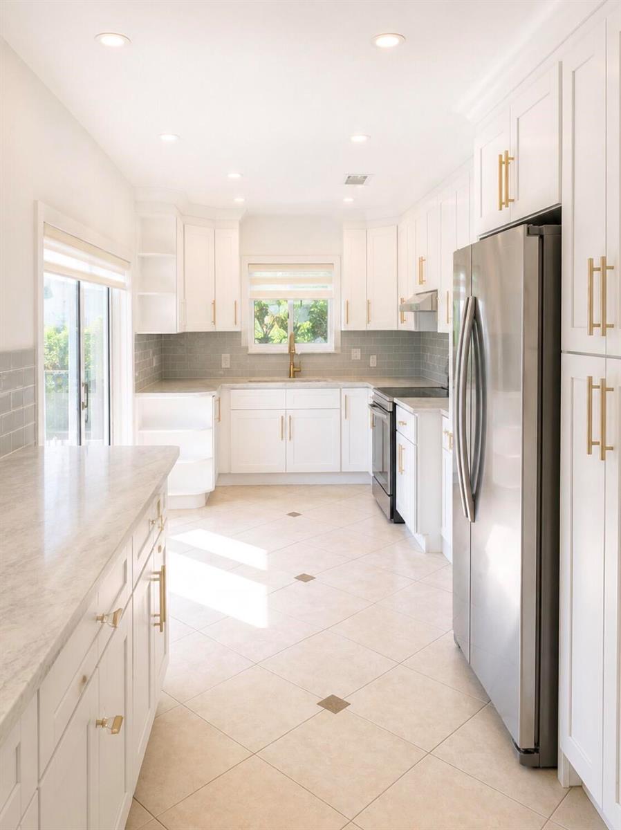 A bright kitchen features white cabinets, gold hardware, stainless steel appliances, and light tile flooring — 7971 Chula Vista Crescent, Boca Raton FL 33433, BOCA RATON, FL