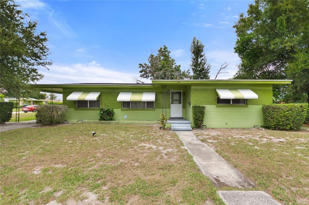 A single-story lime green brick house features white striped awnings over the front windows — 601 AVENUE U NE, WINTER HAVEN, FL