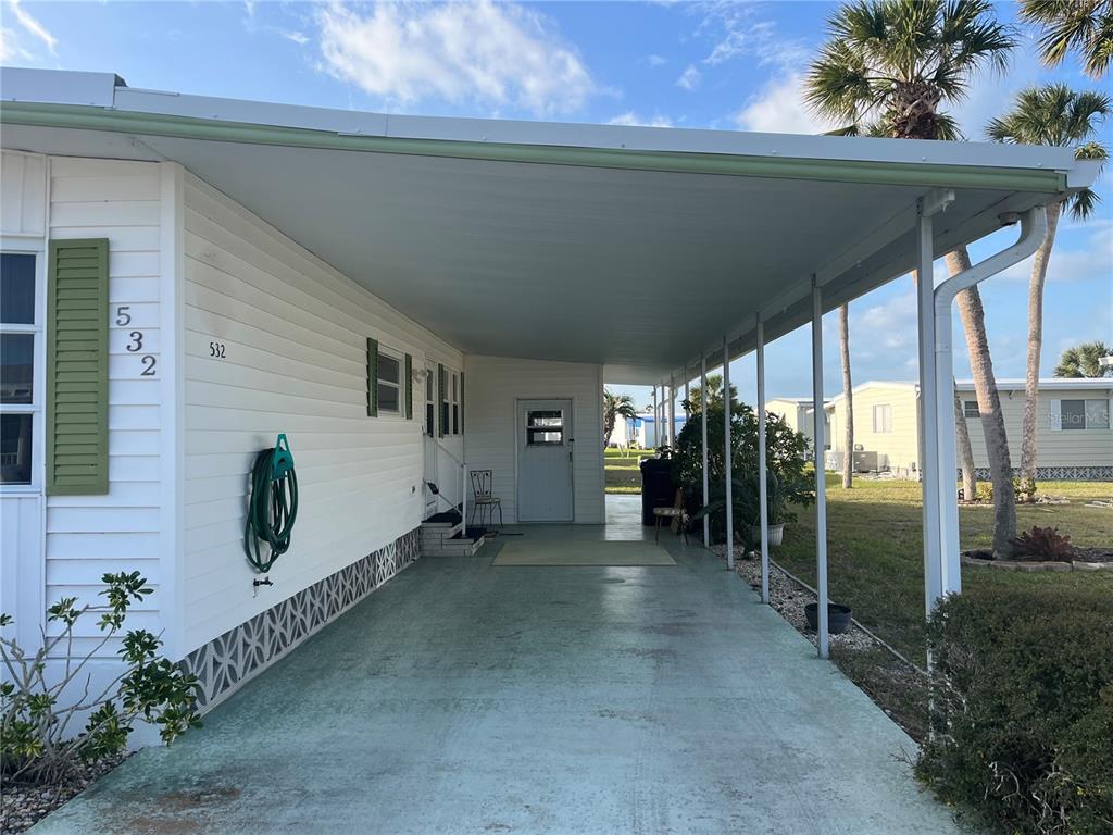 A white mobile home features a long covered carport and a green painted concrete driveway — 532 VIA VENETO, VENICE, FL